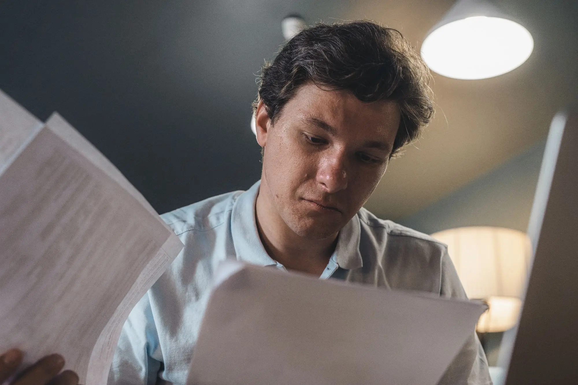 Company director reading through printed loan and tax papers at a desk under a warm lamp