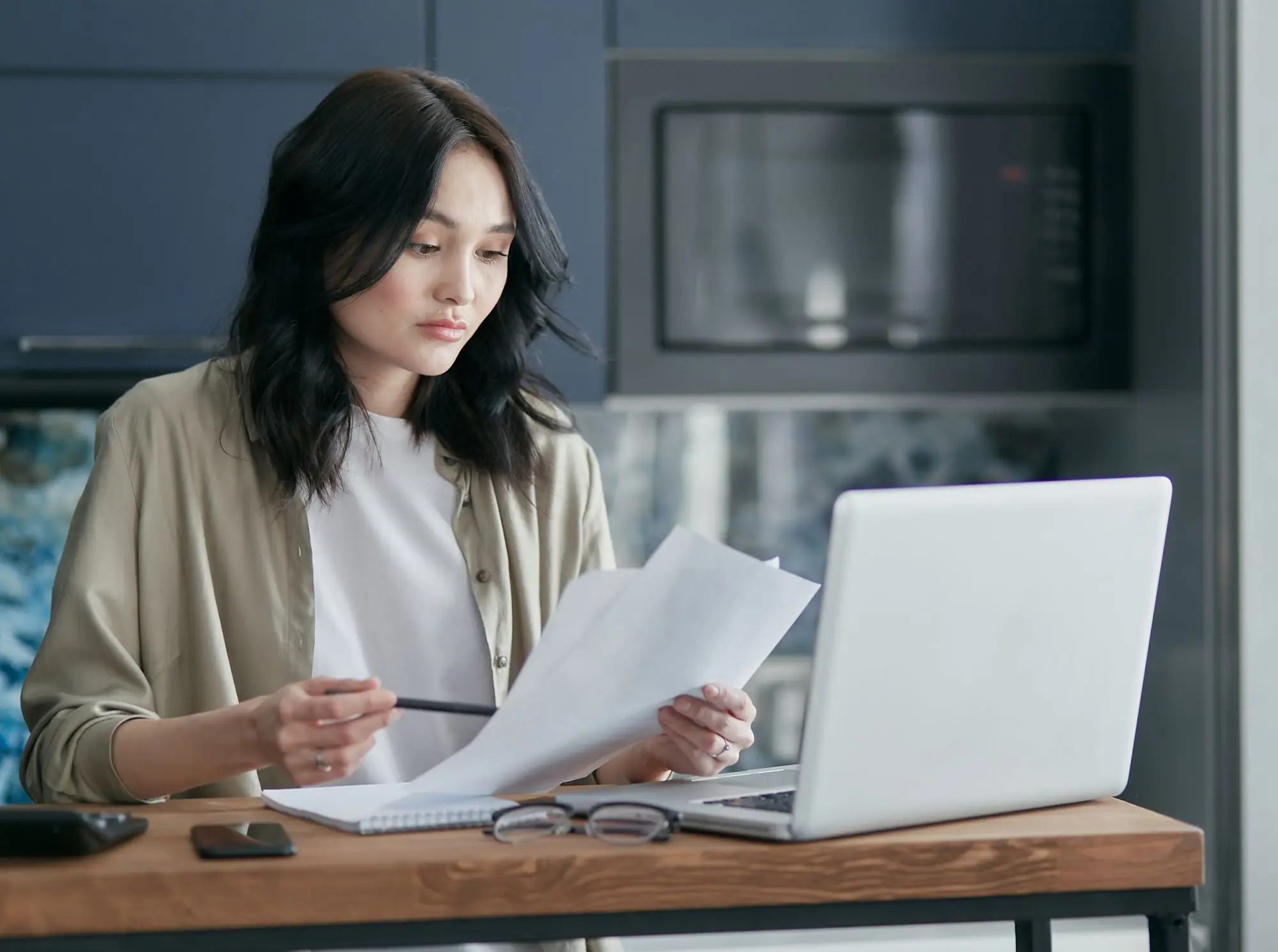 Business owner at her kitchen-table office re-checking printed GST return figures beside a laptop